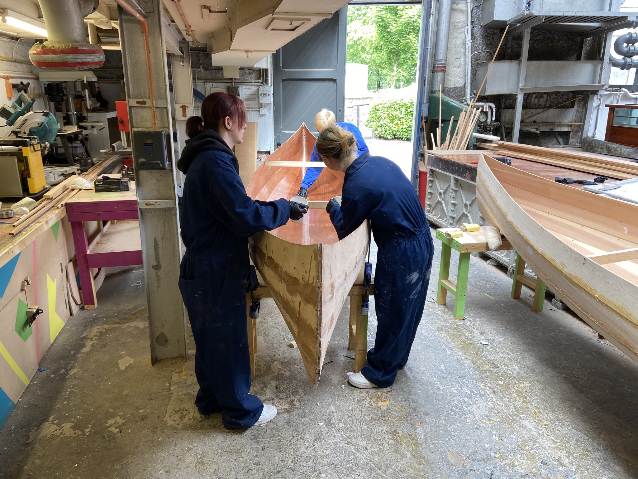 Two young women work on a wooden canoe in a boat workshop