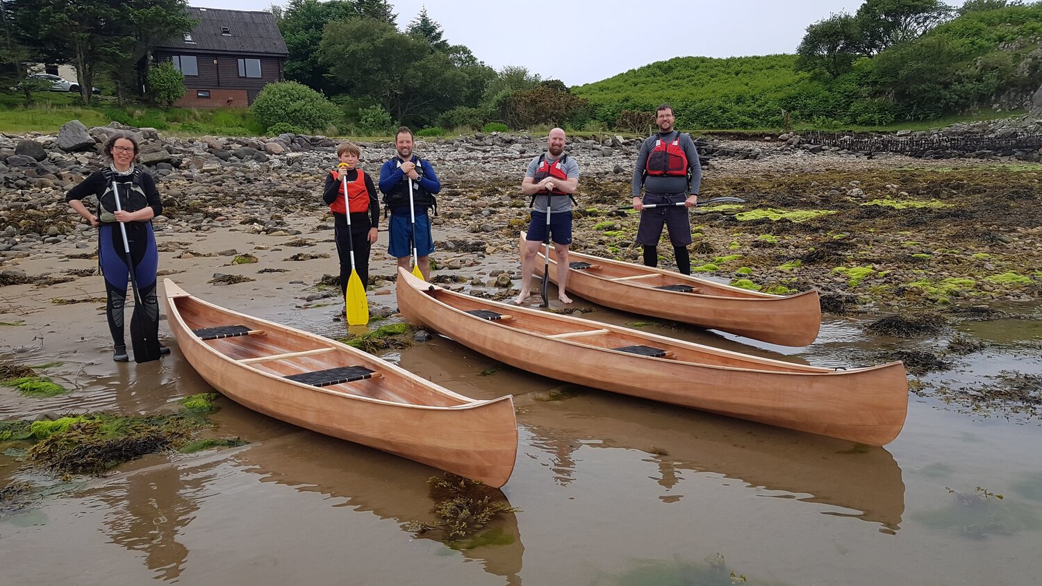 Five people standing next to three newly built wooden canoes
