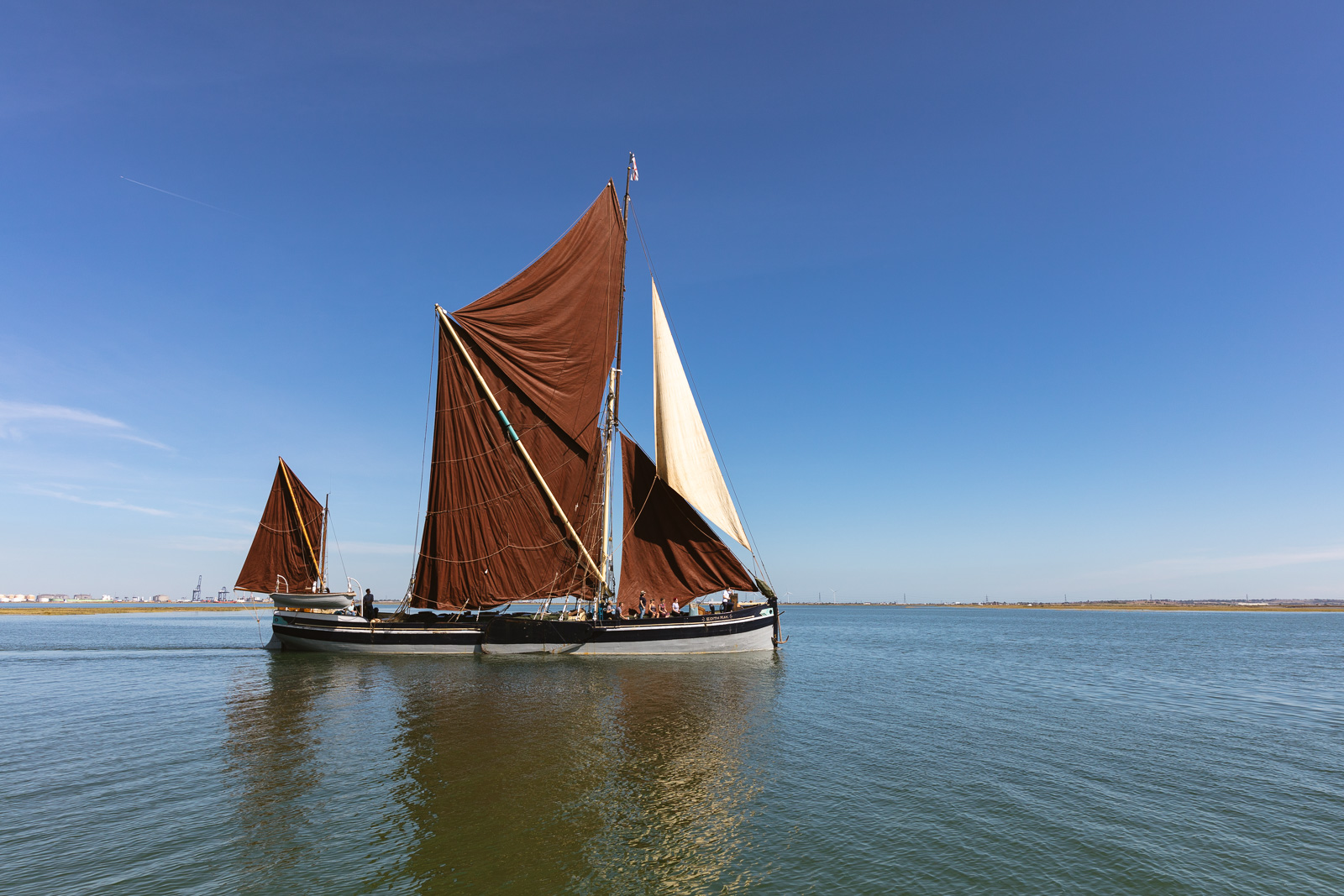 A sailing barge with red sails is crossing a calm area of water