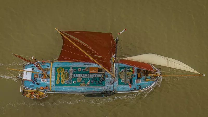 A bird's eye view on SB Cambria with all her sails set, set against the backgruond of green muddy water