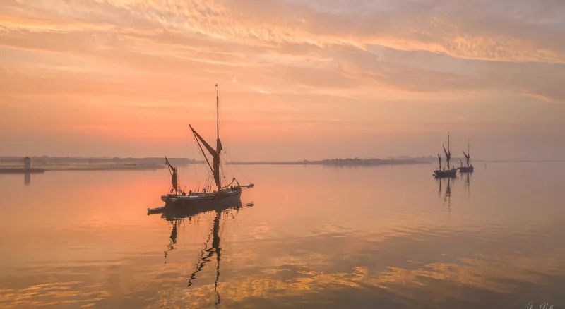 Orange hues dominate the image, most of it is covered by sky and water. In the centre left a bowsprit barge is anchored, with two more barges in the background to the left. The titular Pudge is the furthest away one from the viewer.