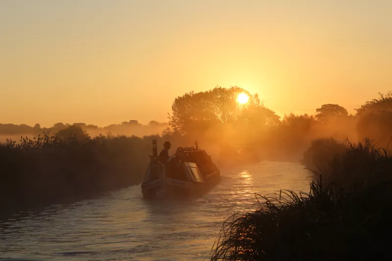 Two narrow boats on the canal enshrined in yellow-hued early morning fog 