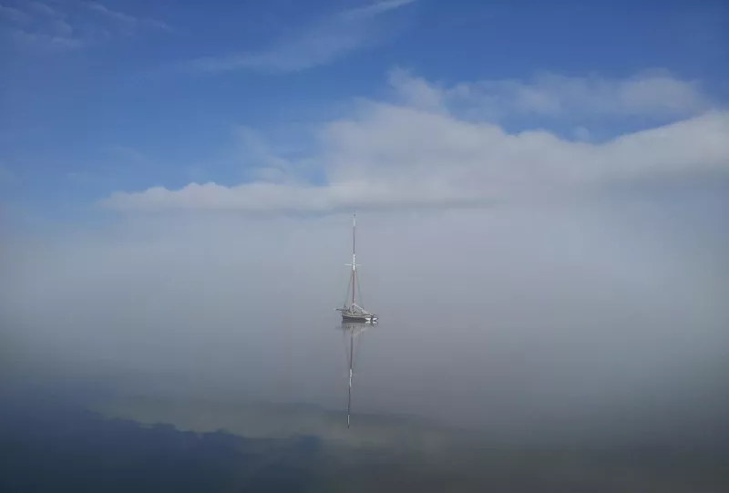 Distant view of a small vessel, the sky and the ship reflected in the smooth water