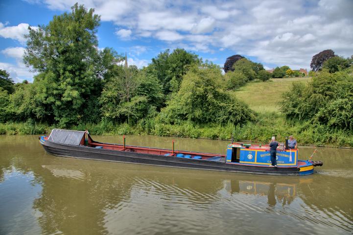 Photo Competition 2023 - Narrow boat Cassiopeia cruising along the Grand Union Canal with the spire of Braunston's St. Bartholomew's Church as a backdrop by Kev Maslin